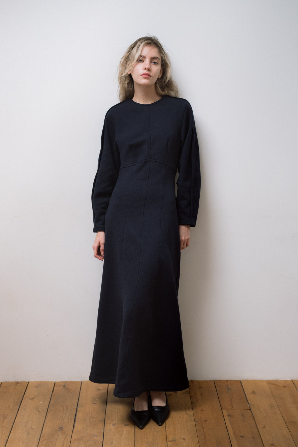 Woman wearing a dark blue dress standing against a white wall.